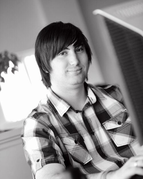 Black and white photo of Craig smiling at the camera from his desk